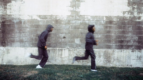 Two people running against a textured wall.